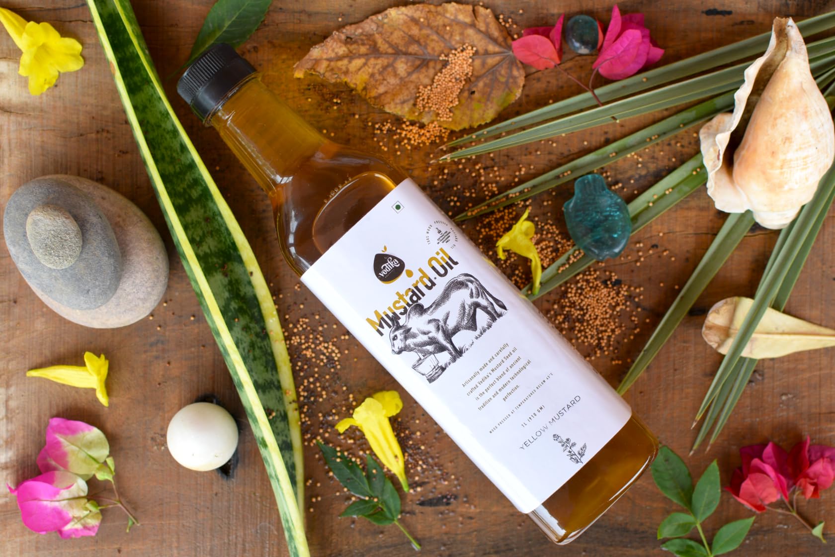Vedika Organics extra virgin yellow mustard oil bottle with mustard seeds flowers and natural ingredients wooden background